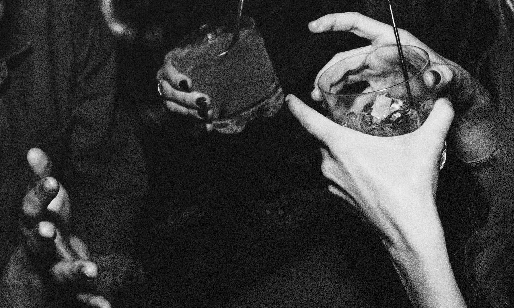 black and white close up of hands holding cocktail drinks